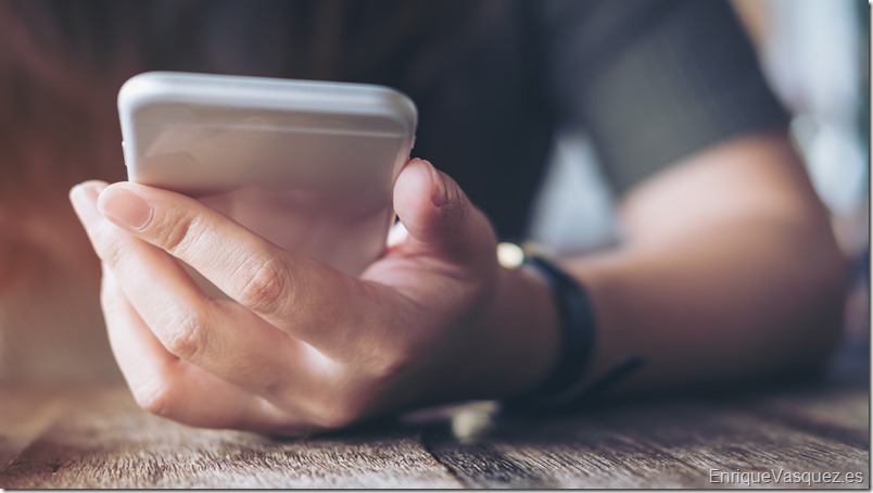 Closeup image of a woman's hand holding and using at smart phone on wooden table in vintage cafe