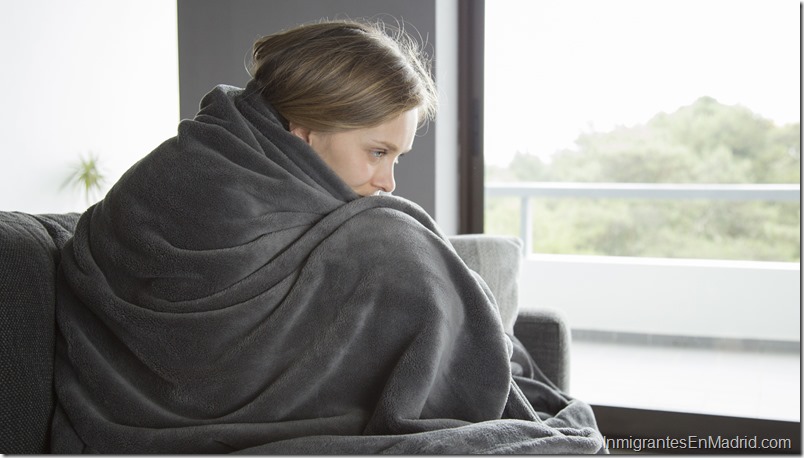 Sick woman sitting on sofa, embracing her knees, thinking