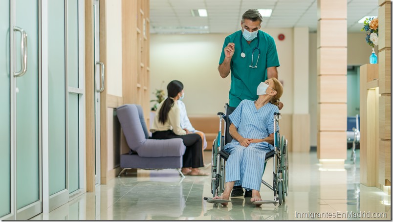 Senior man doctor take care elderly woman patient sitting on a wheelchair at hospital. They are waring face mask for protect coronavirus or COVID-19 disease